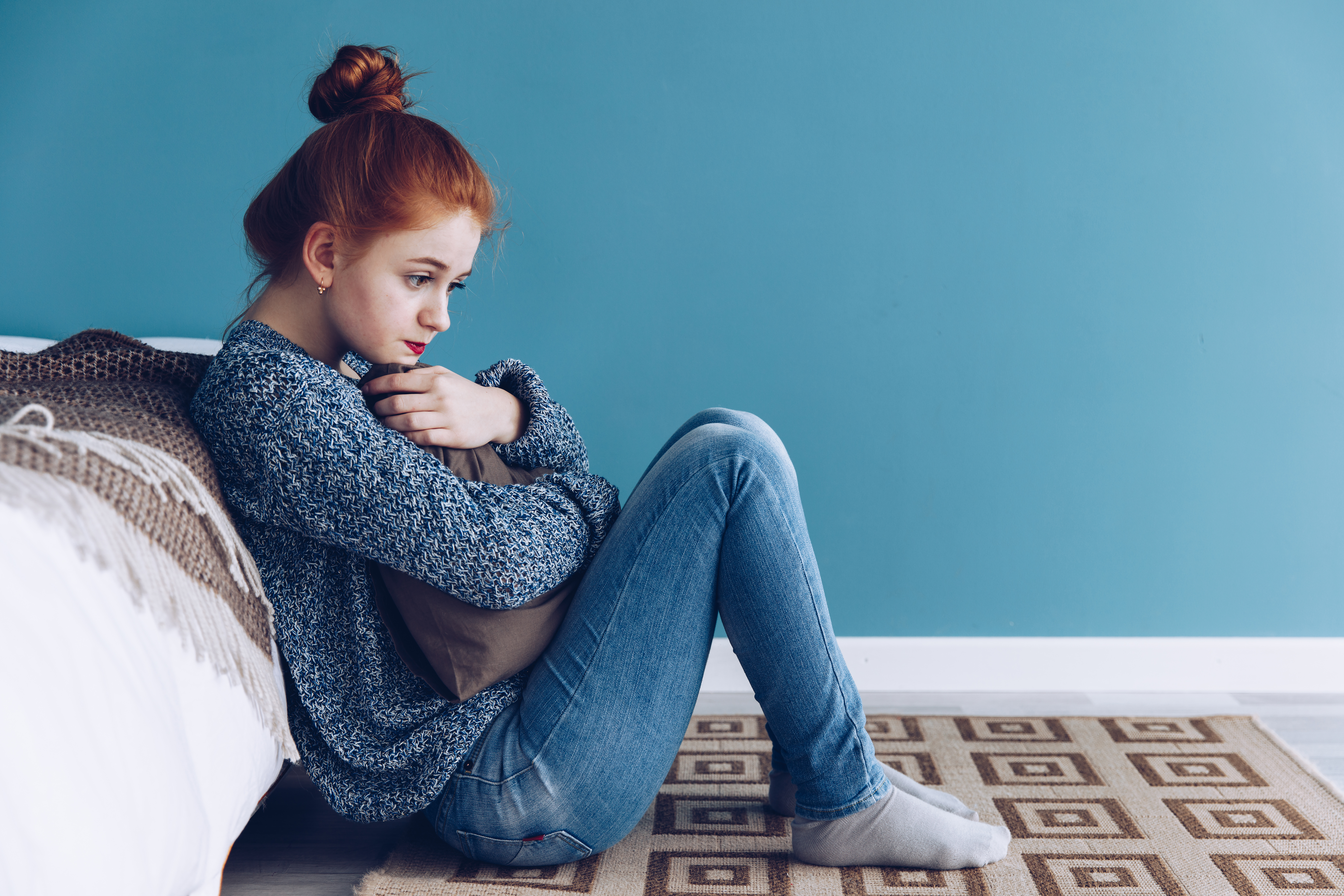 Woman sitting against bed looking downcast
