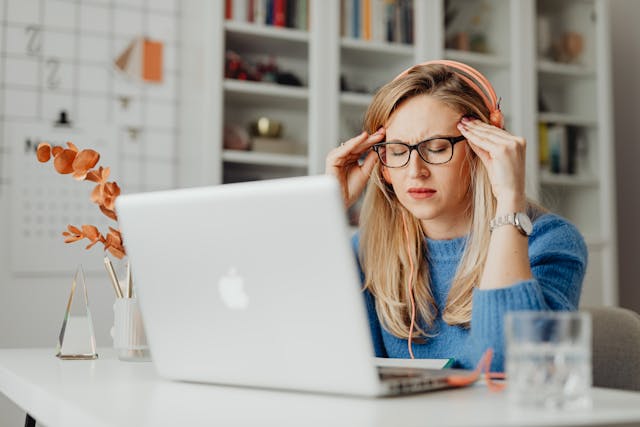 Woman at laptop with hands on temples and eyes closed