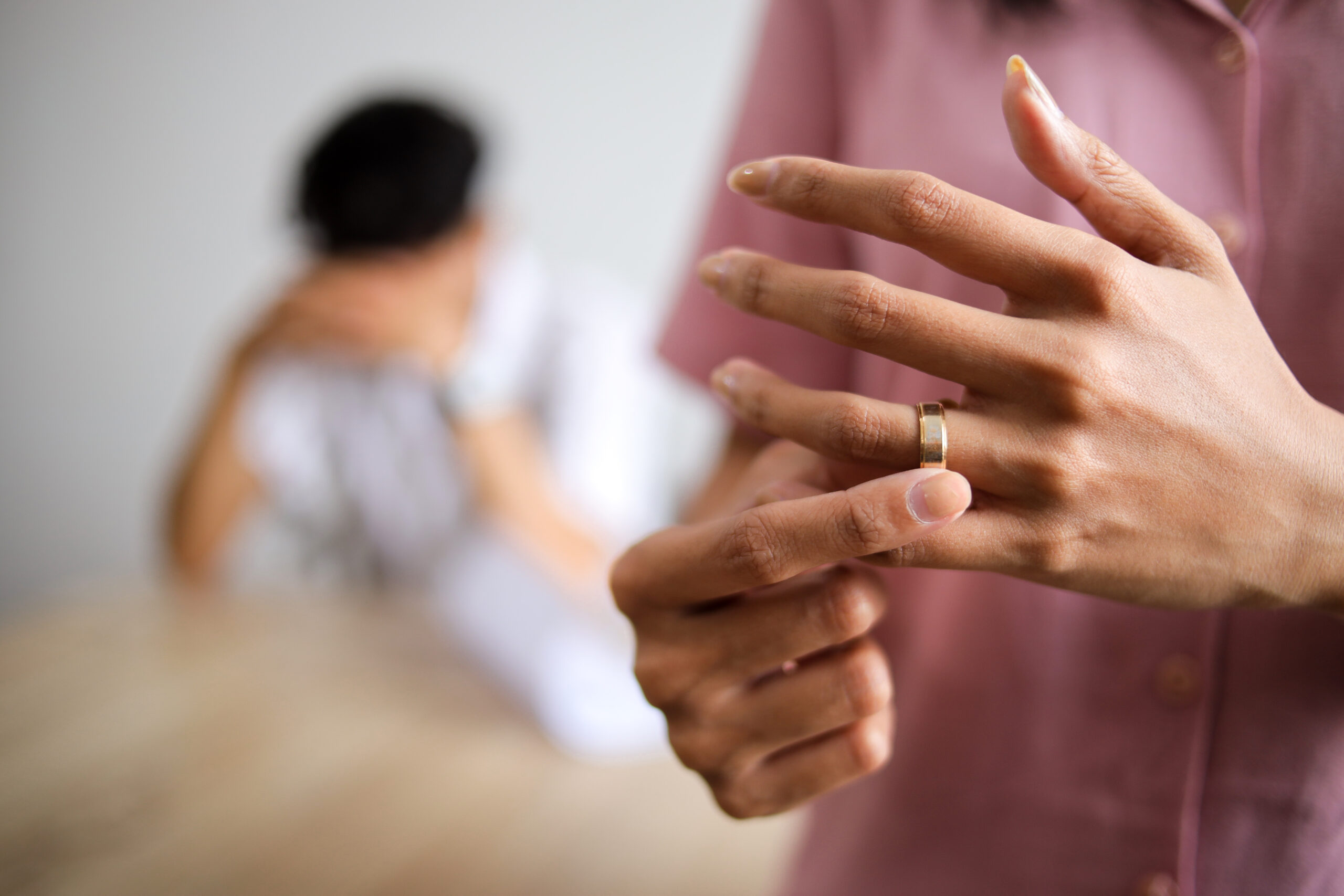 Emotional woman holding ring near distant husband, symbolizing possible separation.