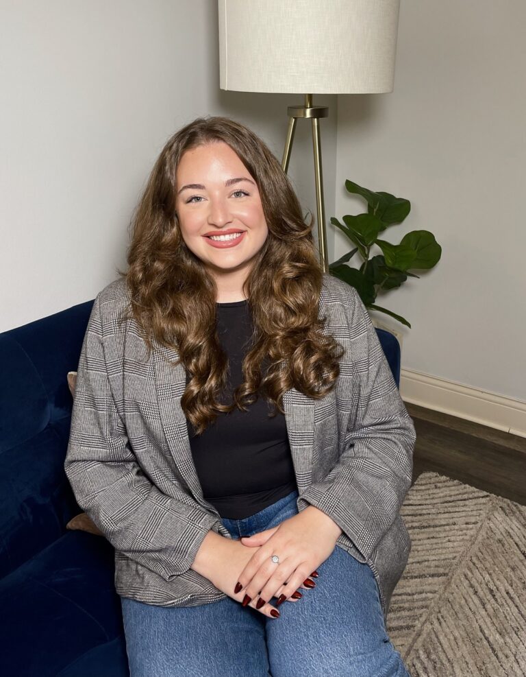 Anamarie Johnson smiling on a blue sofa beside a floor lamp and plant