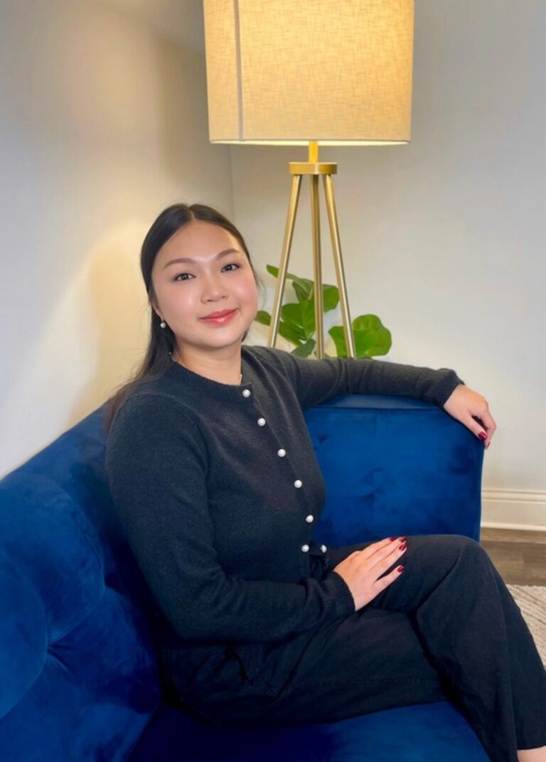 Christy Tran, LPC, smiling on a blue sofa beside a plant and floor lamp