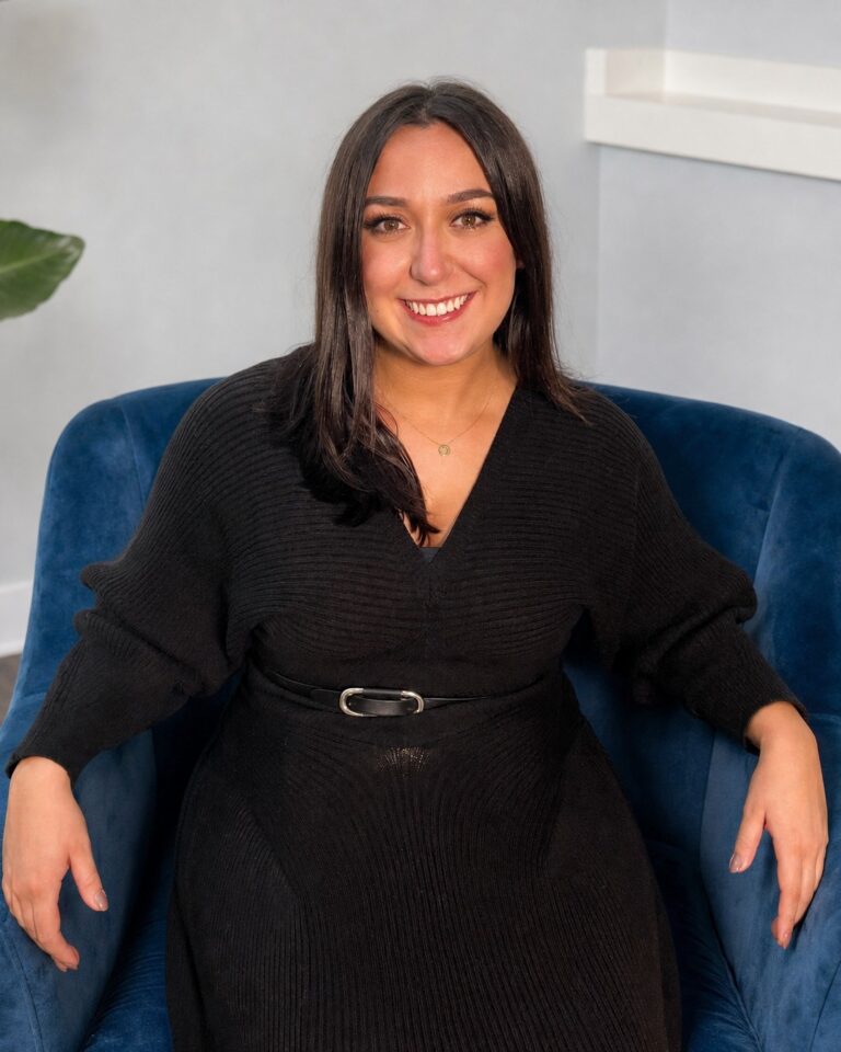 Kathryn Urrutia smiling in a blue armchair beside a large plant
