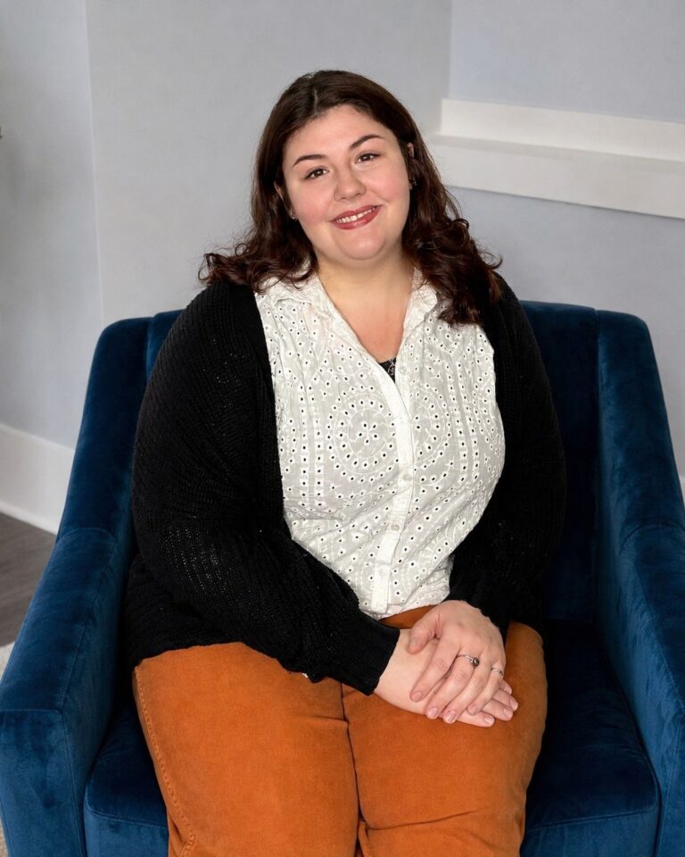 Madeline Bolin smiling in a blue armchair beside a large plant