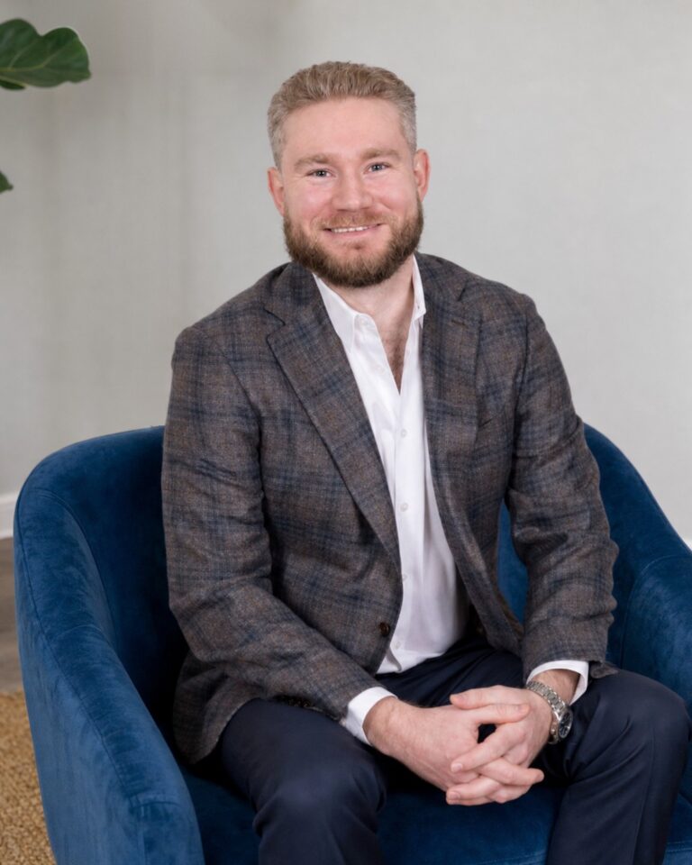 Sam Curry, LPC, smiling in a navy blue armchair in a bright therapy office