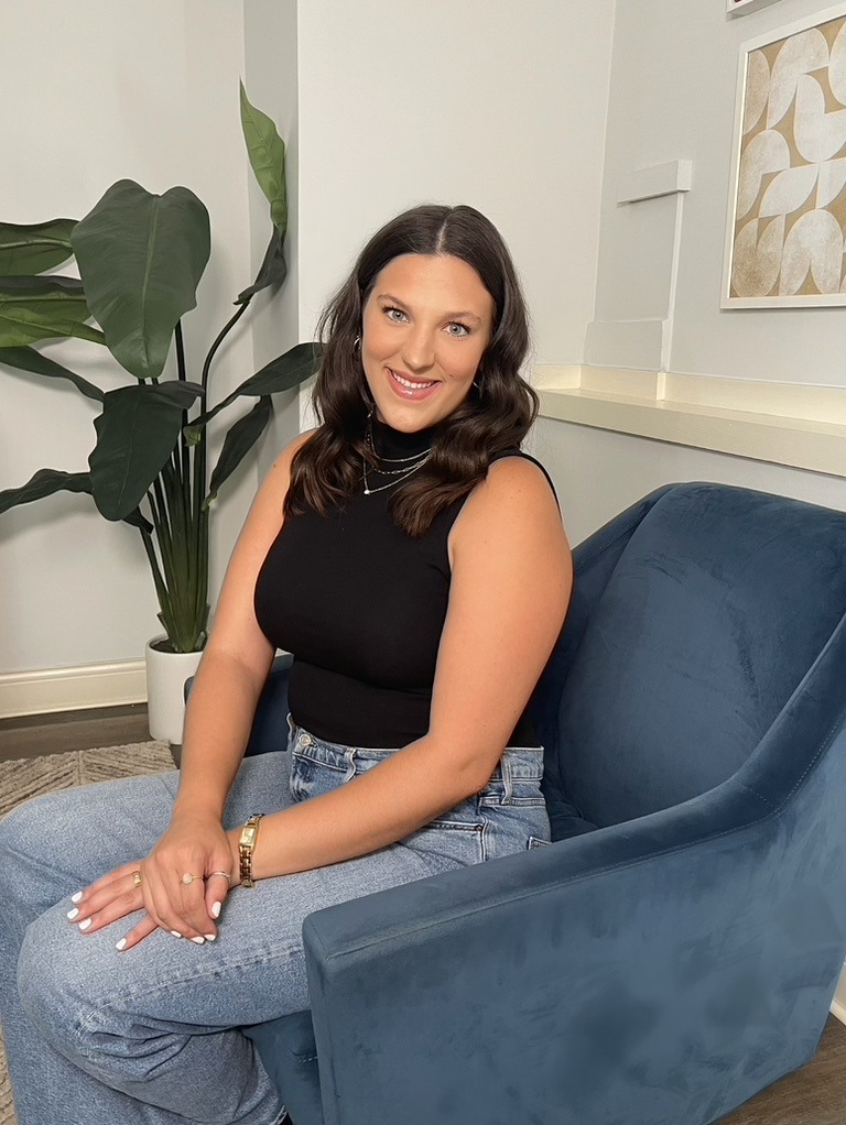 Skyler Whitehead, LSW, smiling in a blue armchair beside a large plant