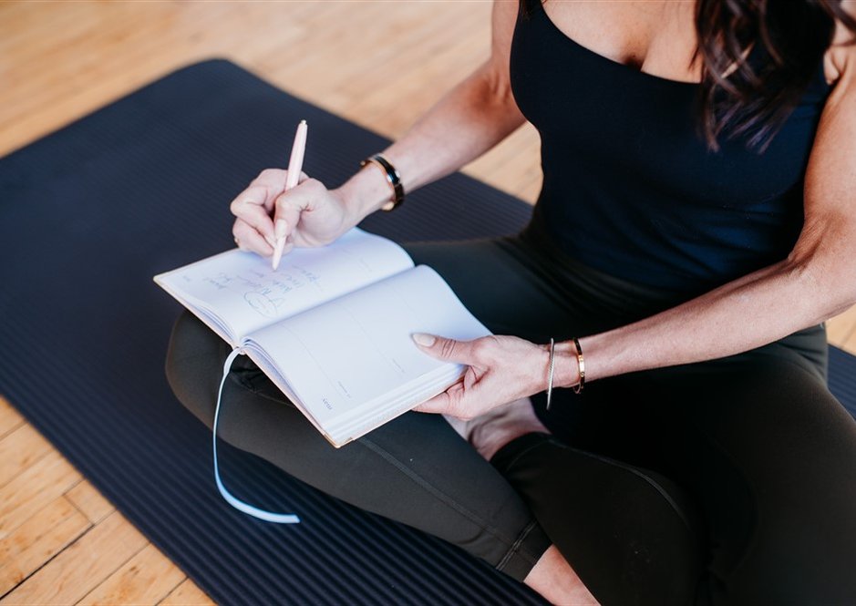 Hands writing in a journal on a yoga mat