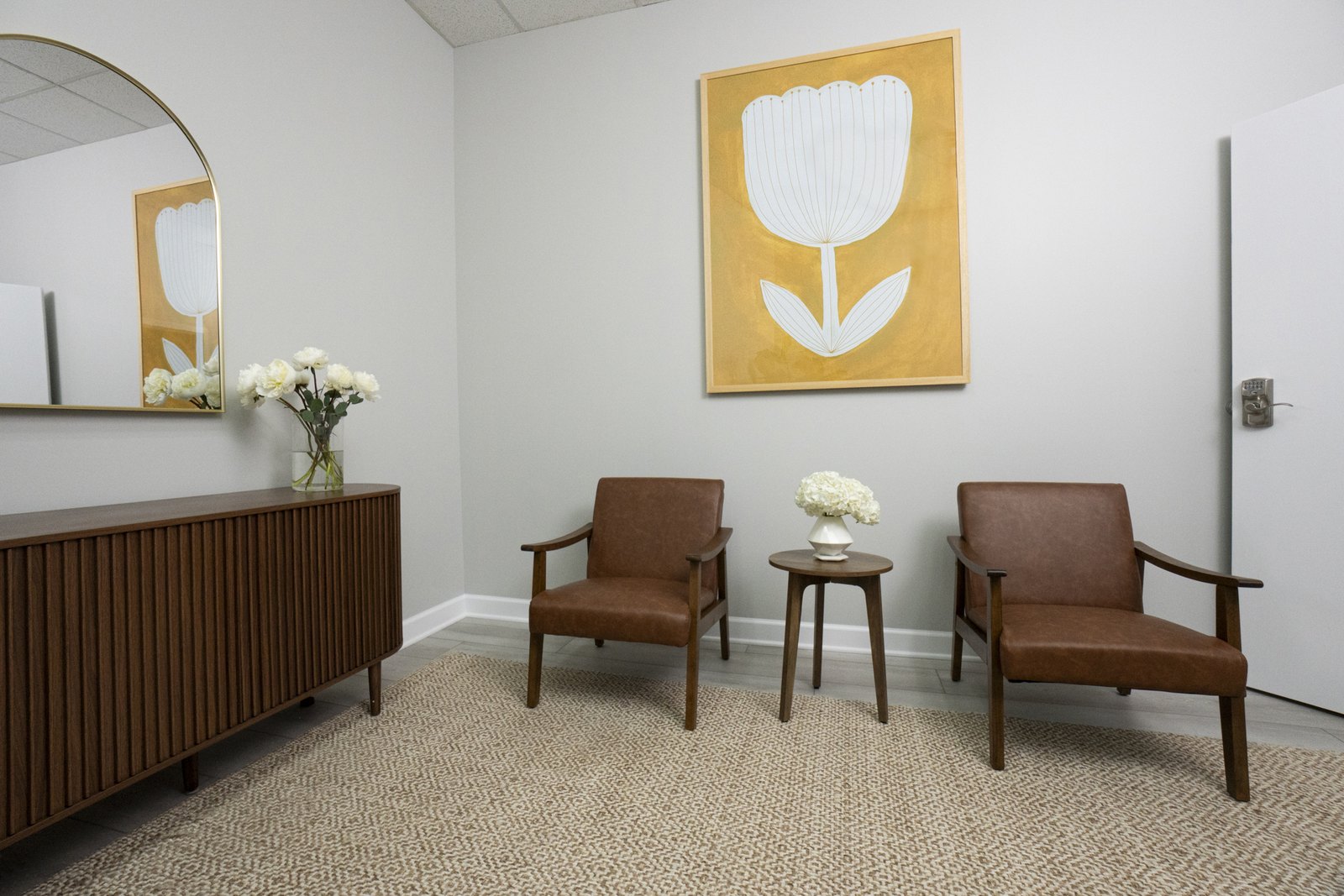 A bright therapy room with a yellow tulip painting and two brown leather chairs