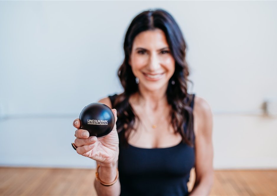 Nicolle Osequeda smiling and holding a Lincoln Park Therapy Group stress ball in a bright room