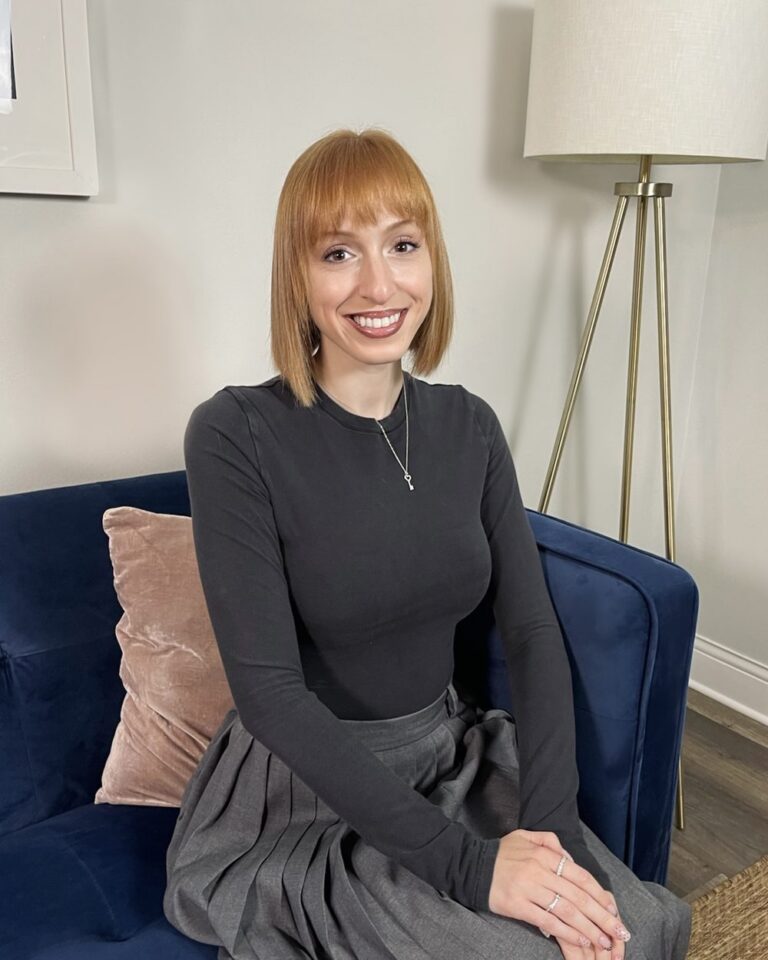 Jessica Katz, LCSW, smiling on a navy sofa beside a lamp in a bright therapy office