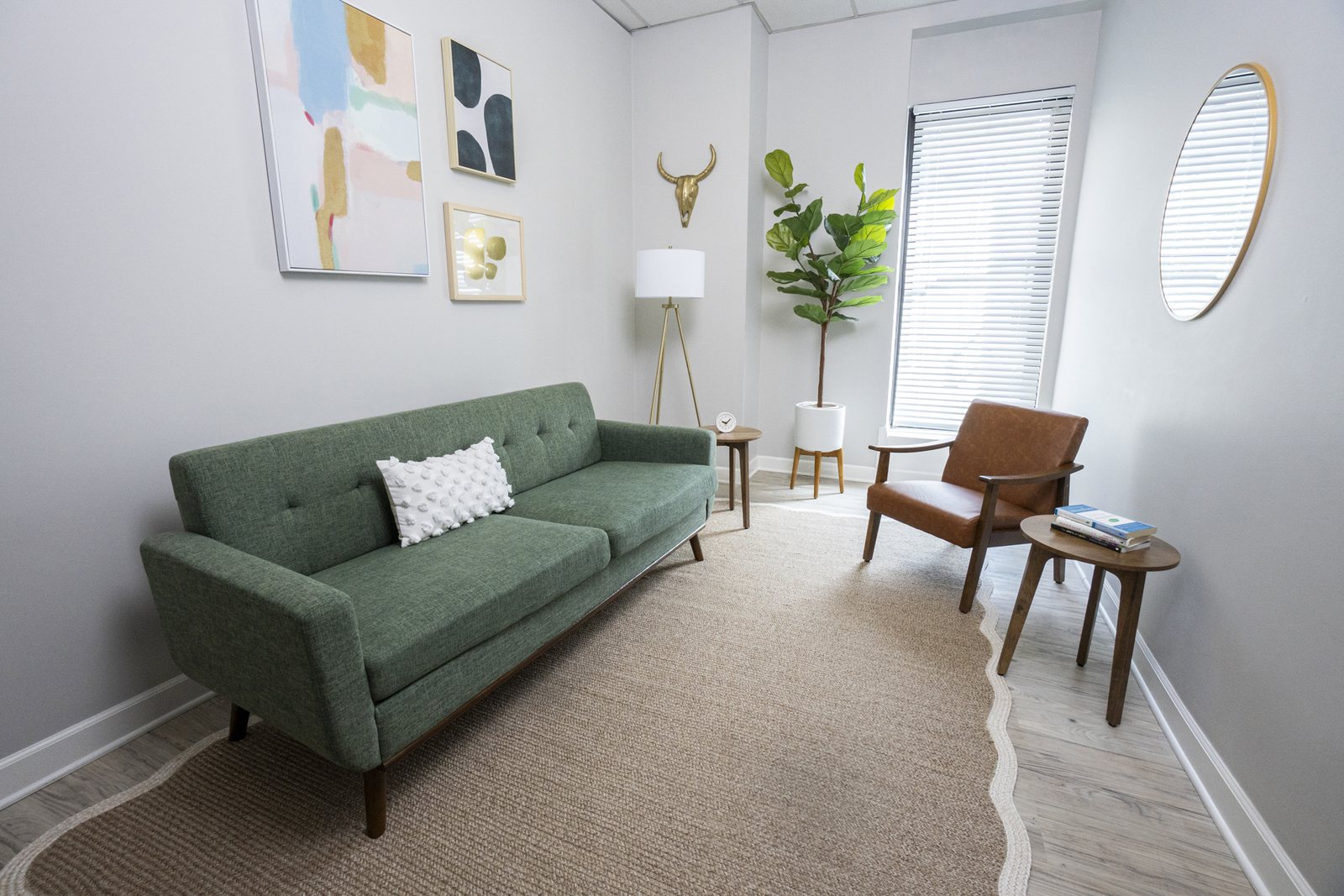 A bright therapy room with a green sofa, leather chair and fiddle leaf fig