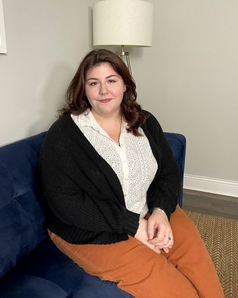 Madeline Bolin smiling on a navy sofa beside a lamp in a bright therapy office