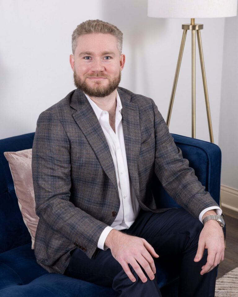 Sam Curry, LPC, smiling on a navy sofa beside a lamp in a bright therapy office