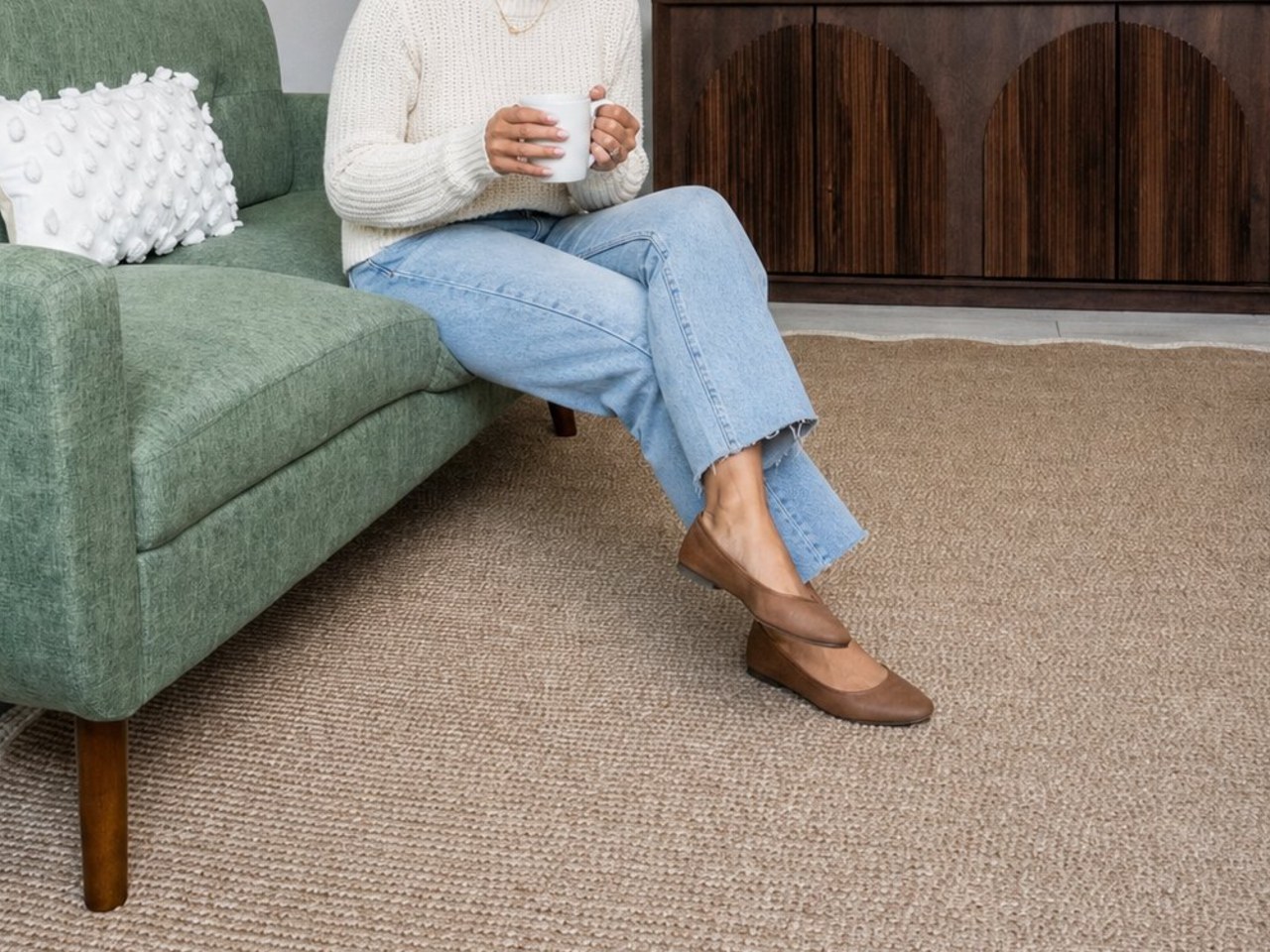 Woman in a cream sweater holding a mug on a sage green sofa in a bright Lincoln Park Therapy Group office